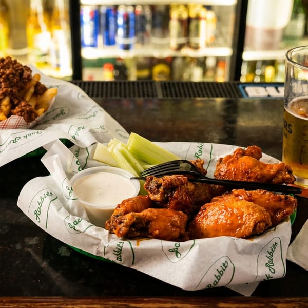 Chili cheese fries, buffalo wings with ranch and celery, and a beer on a bar counter.