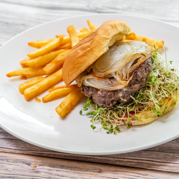 Gourmet burger topped with grilled onions and sprouts, served with golden fries on a white plate.