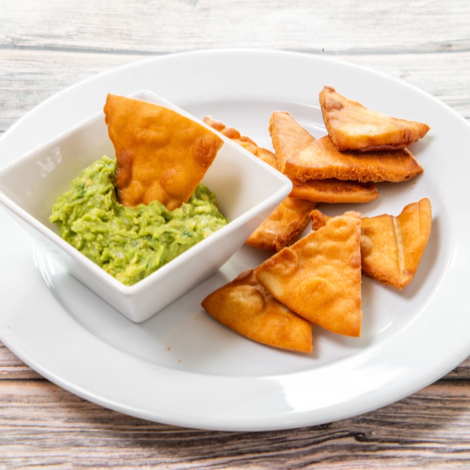 Crispy golden tortilla chips served with a bowl of chunky green guacamole on a white plate.