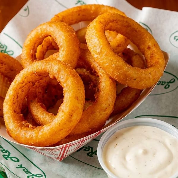 Golden-brown onion rings in a paper tray with a side of dipping sauce on Jack Rabbits branded paper.