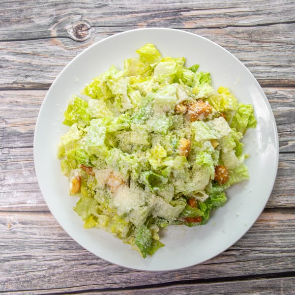 Caesar salad with romaine lettuce, creamy dressing, grated Parmesan, and croutons on a white plate.