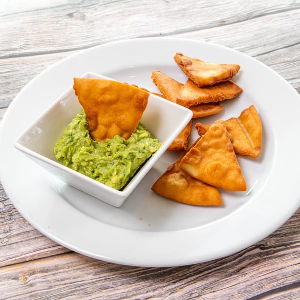 Golden fried tortilla chips served with chunky guacamole in a white bowl on a plate.