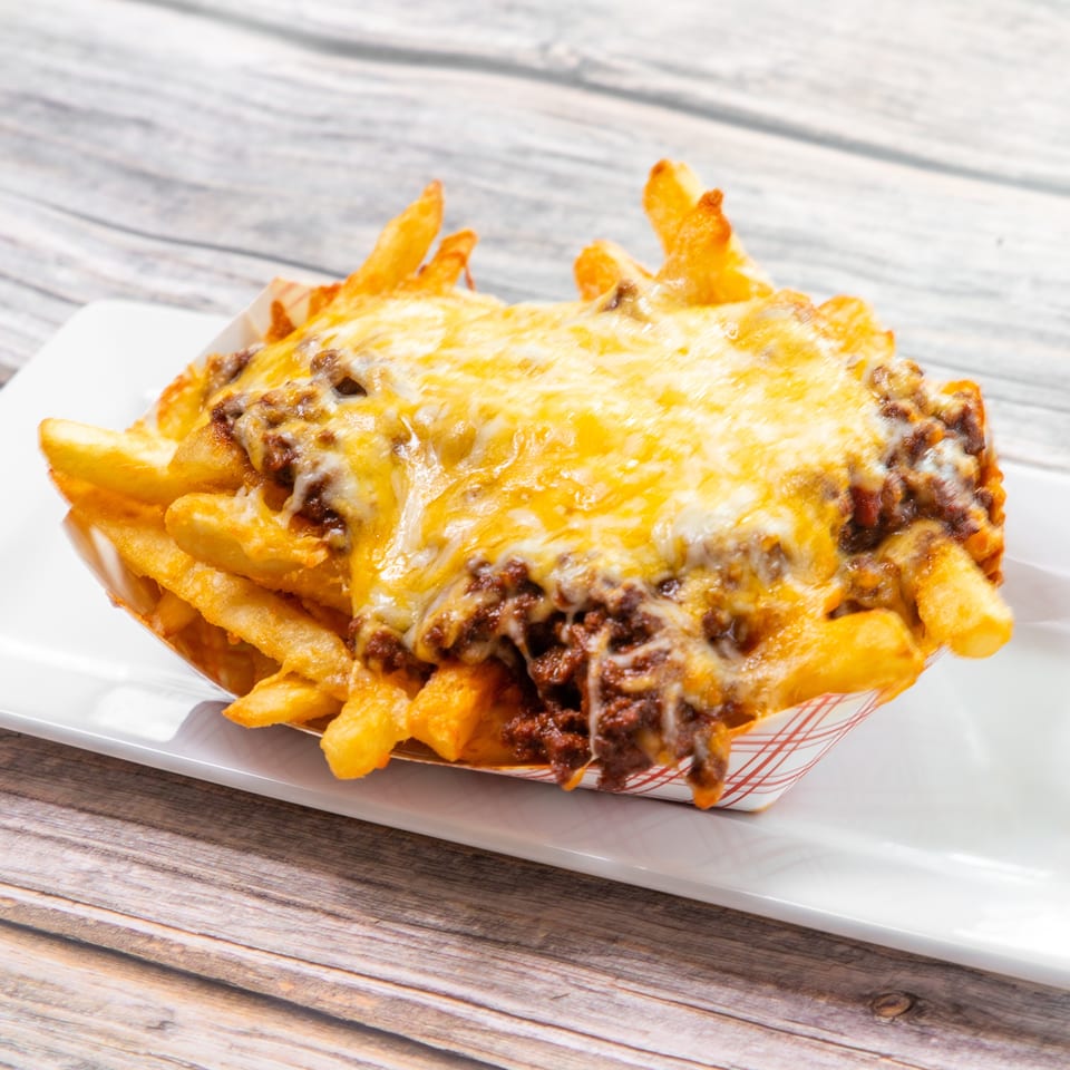 Crispy fries topped with seasoned ground beef and melted cheddar cheese, served in a paper-lined basket on a white plate.