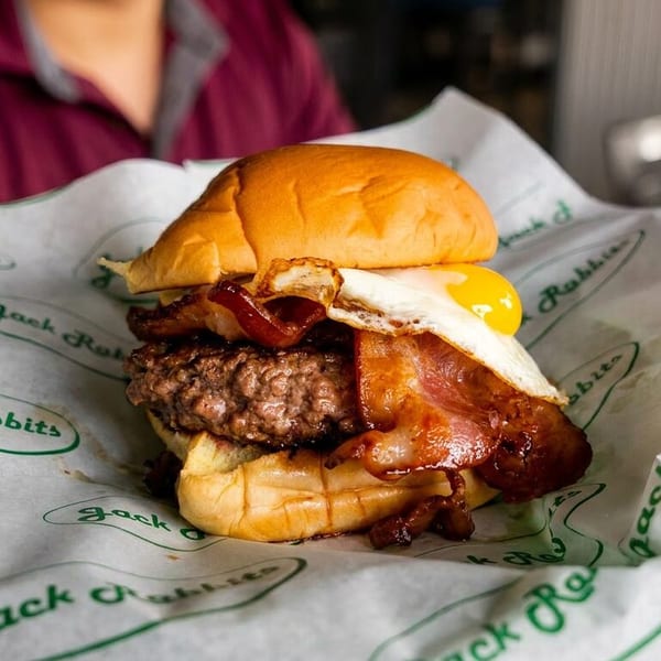 A Jack Rabbits burger with bacon and a fried egg, served on branded paper.
