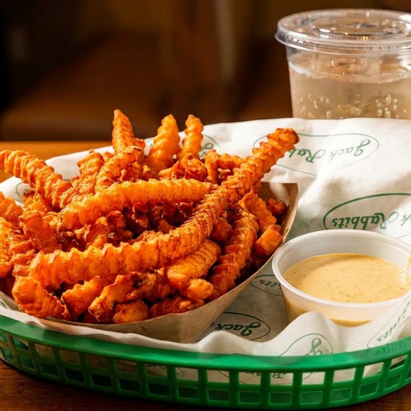 A green basket of crispy curly fries with a side of dipping sauce and a drink.