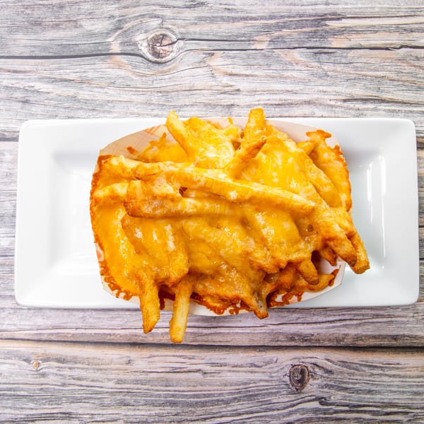 Golden battered vegetable fries piled on a white rectangular plate atop a rustic wooden table.