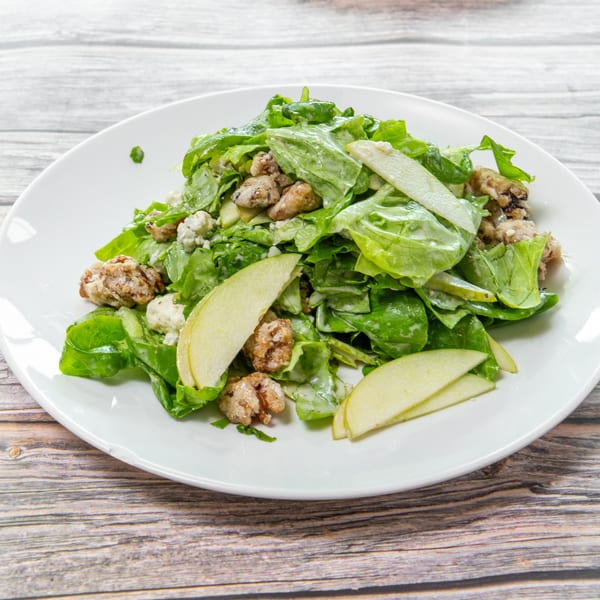 Green leaf salad with sliced pears, blue cheese, and candied nuts on a white plate.