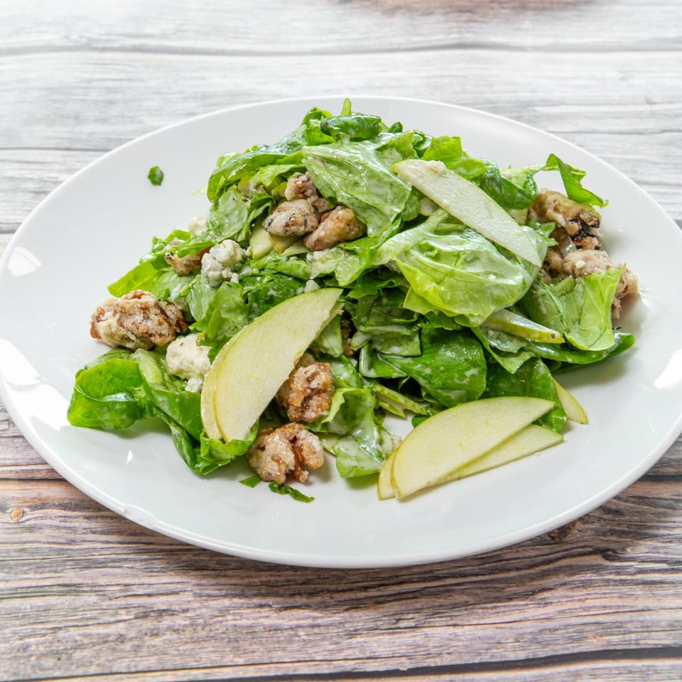 Green leaf salad with sliced pears, blue cheese, and candied nuts on a white plate.